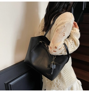 Detail of black matte leather tote bag with elephant charm and long shoulder straps