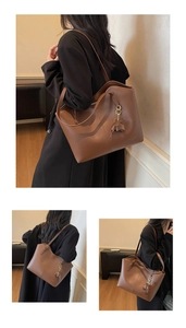 Detail of a brown leather tote bag featuring slim shoulder straps and a floral pendant charm