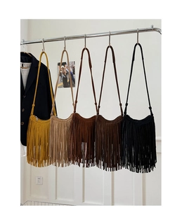 Row of five fringe crossbody bags in yellow brown and black hanging on a metal rack