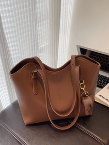 Brown vintage faux leather tote bag with elephant charm on a leather bench seat