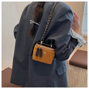 Detail of mustard yellow quilted chain bag with flower logo and dual zippers on a model