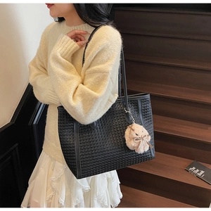 Detail of black woven tote bag with brown plush pom-pom charm on wooden steps