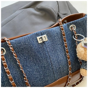 Macro view of denim patchwork tote with silver turn-lock and teddy bear charm