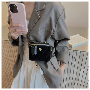 Detail of black velvet quilted box bag with gold flower logo on a grey blazer outfit