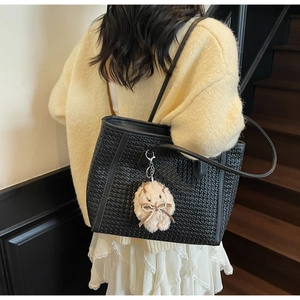 Detail of black woven tote bag featuring a cute white plush bunny charm and leather straps