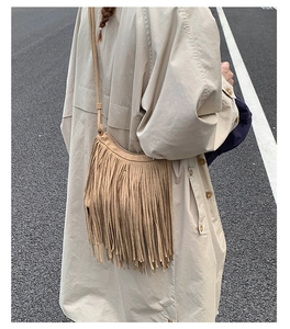 Outdoor street view of a bohemian khaki fringe crossbody bag with suede texture detail