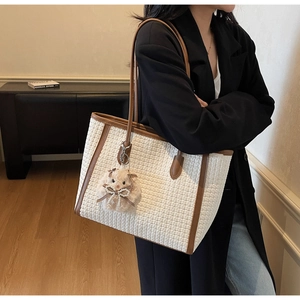 Detail of white woven tote bag with brown leather straps and cute plush animal charm