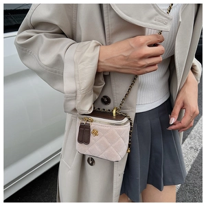 Detail of quilted beige box bag with golden flower buckle and chain strap on a model