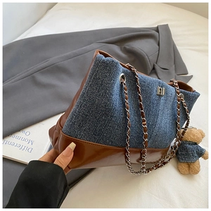 Detail of color-block denim tote with brown leather trim and bear pendant accessory