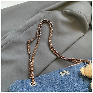 Detail of denim tote bag with brown chain strap, metal twist lock and plush bear charm
