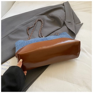 Detail of color-block tote bag featuring blue denim and brown leather with metal chain