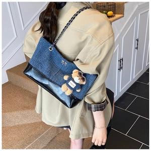 Detail of blue denim and black faux leather tote with chain strap and plush bear charm