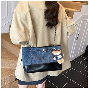 Detail of color-block denim and black leather tote with chain strap and bear charm
