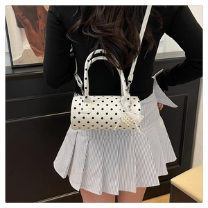 Détail d'un sac polochon blanc à pois porté en bandoulière avec breloque en dentelle