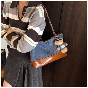 Detail of denim patchwork tote bag with chain strap and cute bear charm on model