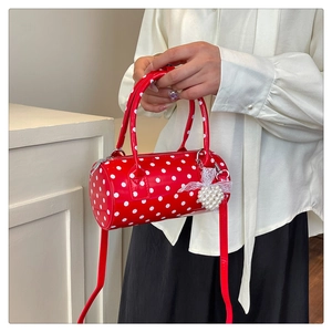 Gros plan du sac cylindrique rouge à pois avec fini brillant et breloque cœur en perle