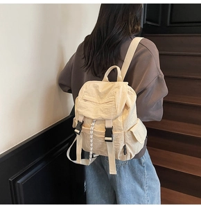 Detalle de la mochila de nailon beige con solapa de hebilla, cordón y bolsillos laterales