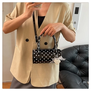 Détail d'un sac cylindre noir brillant à pois blancs avec un charme en forme de cœur