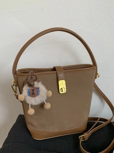 Vintage braune Bucket Bag mit rundem Griff und Plüsch-Anhänger auf weißem Hintergrund