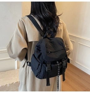 Vista trasera de una mochila de nailon negro con hebillas sobre una gabardina color beige