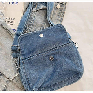 Detailed view of blue denim crossbody bag with silver magnetic buckle and front pocket