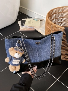 Denim patchwork tote bag with chain strap and teddy bear charm on dark tile background