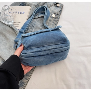 Detailed texture of blue denim crossbody bag placed on casual outfit background