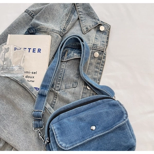 Detail of blue denim crossbody bag featuring a metal buckle and adjustable strap