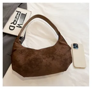 Detailed view of brown suede hobo bag with contrast handle next to fashion book and phone