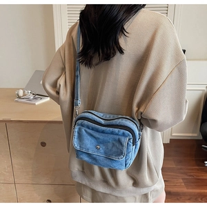 Detail view of a light blue denim crossbody bag worn by a model in a lifestyle setting