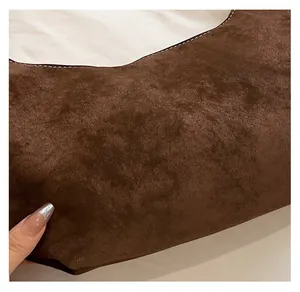 Close-up of brown suede fabric texture with detailed white stitching on a minimalist bag