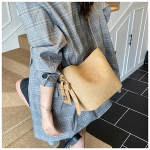 Detail of khaki frosted leather bucket bag with metal lock and side hanging tag charm