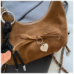 Detail of brown suede crescent bag with silver heart charm and bow accent