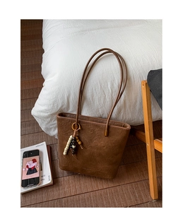 Detail of vintage brown tote bag with pleated texture and ethnic style beaded pendant charm