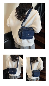 Detail of blue denim crossbody bag featuring multi-compartment zip and silver metal buckle