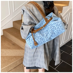 Detail shot of a blue leopard print tote bag with brown leather handles and side charm