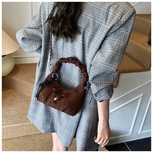 Detail of dark brown suede crescent bag with heart charm and chain strap on shoulder
