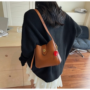 Detail of warm brown bucket bag with gold clasp and red strawberry charm on shoulder