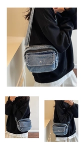 Detail of blue denim crossbody bag featuring double zip compartments and metal buckle