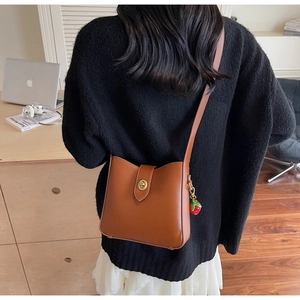 Rear view of a caramel leather bucket bag with a strawberry charm and gold hardware