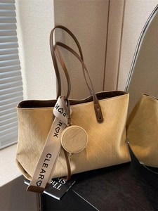 Sand yellow suede tote bag with diamond quilting and decorative ribbon in natural light