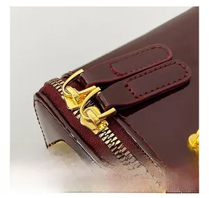 Detailed close-up of wine red patent leather handbag with gold zippers and metal hardware