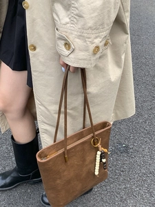 Brown oil wax leather tote bag with wooden bead charm worn with khaki trench coat