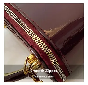 Close-up of smooth gold metal zipper and stitching on a burgundy patent leather handbag