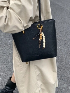 Chic black oil wax leather tote bag with ethnic bead charm shown in street style