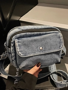 Blue denim crossbody bag with adjustable strap and front pocket held by hand