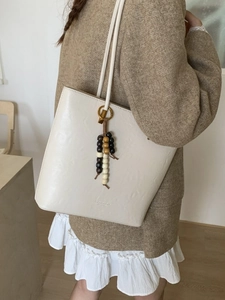 Beige embossed tote bag with retro patterns and wooden bead tassel shown on model