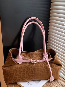 Large leopard print tote bag with pink leather handles and gold buckles on a wooden table