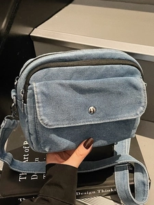 Blue denim crossbody bag with dual zippers and front flap pocket held in hand