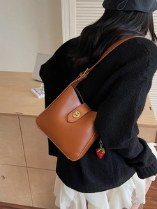 Brown leather bucket bag with metallic twist lock and strawberry pendant on a model